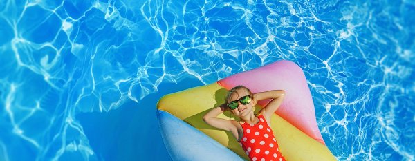 Ein junges Mädchen mit Sonnenbrille liegt auf einer Luftmatratze entspannt im Pool.